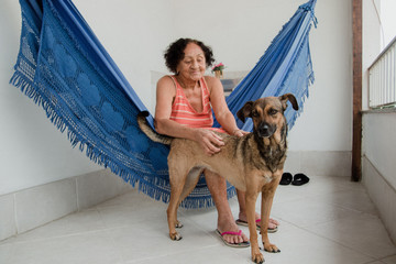 Brazilian elderly woman sitting in a hammock at home with her dog