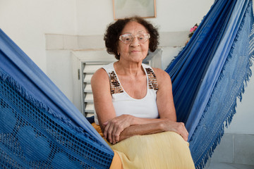 Brazilian elderly woman sitting in a hammock at home