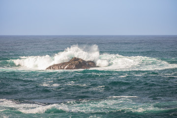 Fototapeta premium Waves breaking on large rock in ocean