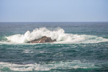 Waves breaking on large rock in ocean