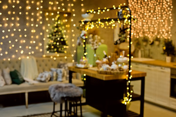 Blurred Christmas background with Christmas tree and lights. A lot of glare and blurred bokeh Golden brown. Kitchen in Christmas lights garlands.