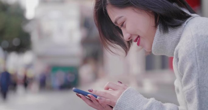 Side view Close up of happy young asian woman using mobile phone browsing social medial in the autumn urban street with blurred background at Chengdu Sichuan China 