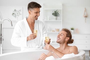 Obraz na płótnie Canvas Happy gay couple drinking champagne in bathroom