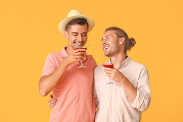 Happy gay couple with cocktails on color background