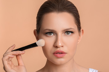 Beautiful young woman applying makeup against color background