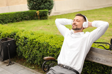 Handsome businessman listening to music while relaxing in park