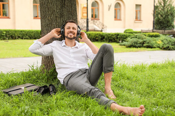 Handsome businessman listening to music while relaxing in park