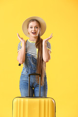 Surprised young woman with suitcase on color background. Travel concept