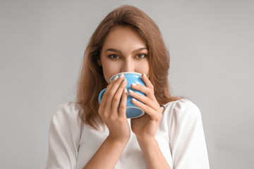 Beautiful young woman with cup of tea on grey background