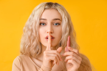 Beautiful young woman with lipstick showing silence gesture on color background