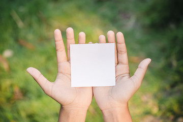 Woman hand holding blank paper on nature background.