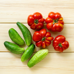 Ripe tomatoes and cucumbers on a light wooden background, top view