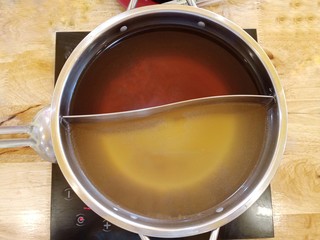 Shabu soup in the shaba pot consists of black water soup and clear soup base, divided in half. Used to boil meat and vegetables before eating on a wooden background.