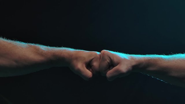 Conflict concept. The clash of two fists of male athletes on a black background. Slow motion. Close up.