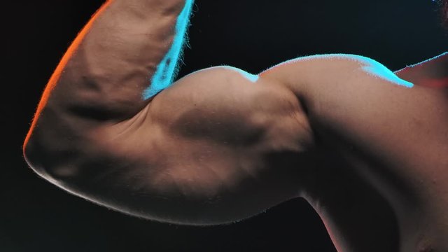 Muscular athlete flex biceps on arm, showing muscles. Concept of sports and body. Shot in the studio on a black background. Slow motion. Close up.