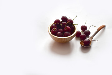 Closeup of Fresh Ripe Cherries in a wooden bowl and wooden spoon with water drops isolated on white background.