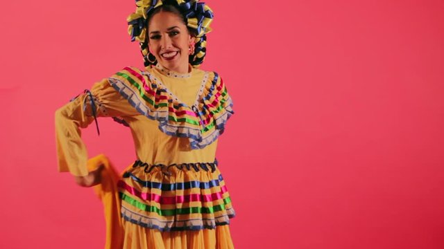 Joven mujer mexicana latina en traje regional folclórico en fondo rosa haciendo orlas con vestido baile danza típico girando