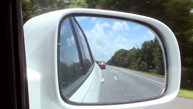 View of highway passing by through side mirror of a car.