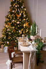 Christmas or New Year festive table setting. The festive wooden dining table is decorated with spruce garland and white candles. Christmas gift on a plate.