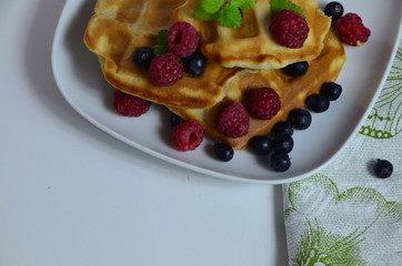 Homemade Belgium Waffles with fresh blueberries for breakfast. White plate, Viennese waffles with raspberries and mint. quick delicious breakfast on white background