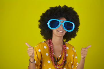 Young beautiful and smiling girl with curly afro hairstyle and funny glasses showing thumbs