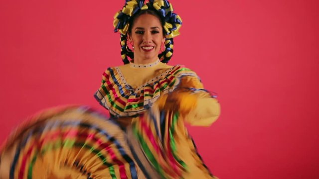 Joven mujer mexicana latina en traje regional folcl&oacute;rico en fondo rosa bailando