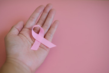 A pink ribbon on woman hand isolated on pink background with copyspace. Breast cancer awareness symbol for supporting people living and illness. International Women day and World cancer day concept