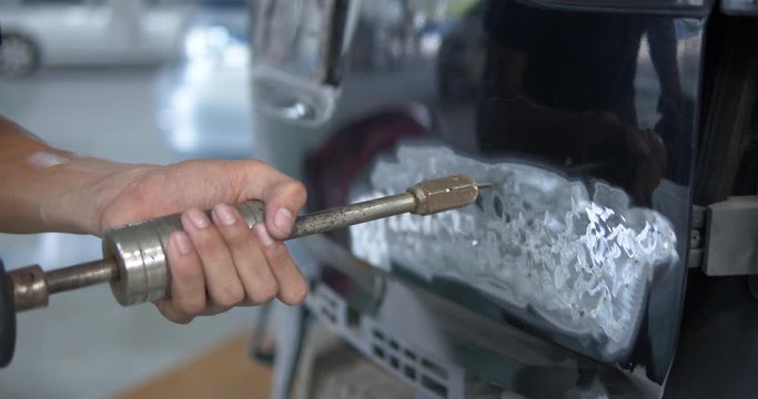 Car body repair with spotter. Mechanic's hands straighten the auto body part repair.