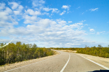 Naklejka premium View from car windscreen with stripe relief to highway, tundra and blue sky in norht region at a sunny day