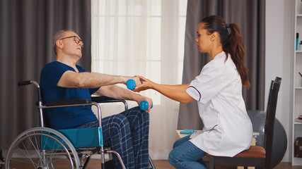 Doctor helping senior man in wheelchair with muscle rehabilitation exercise. Disabled handicapped old person with social worker in recovery support therapy physiotherapy healthcare system nursing