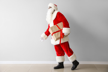 African-American Santa Claus with gift near light wall