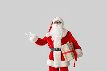 African-American Santa Claus with gift on light background