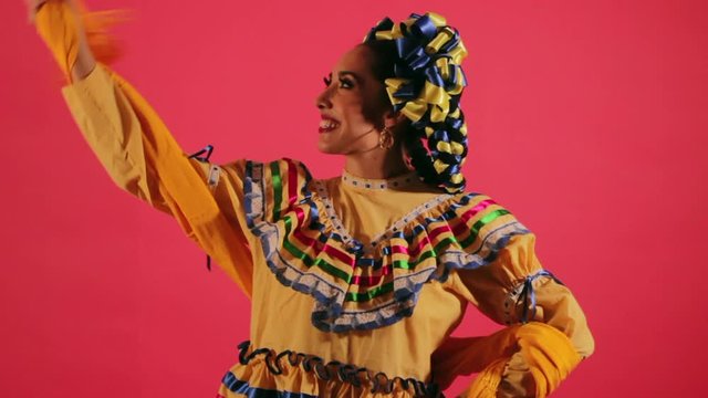 Joven mujer mexicana latina en traje regional folclórico en fondo rosa arreglando su vestido feliz contenta