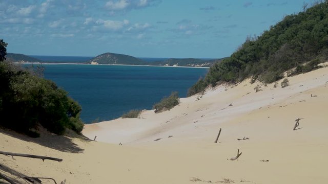 Peaceful summertime screensaver scene of Carlo Sand Blow at Cooloola with blue ocean sea water at Rainbow sandy beach with dunes in background on bright sunny sky day, Queensland, Australia, static