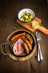 Oldenburger Grünkohl mit Pinkel, Kohlwurst, Kassler Schweine Nacken, Senf und Kartoffeln in Gusseisen Pfanne auf Holz Tisch