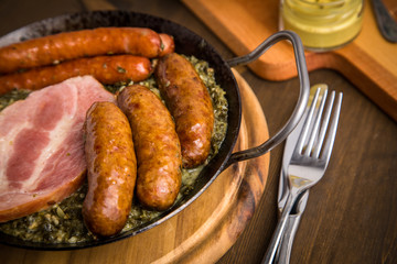 Oldenburger Grünkohl mit Pinkel, Kohlwurst, Kassler Schweine Nacken und Senf in Gusseisen Pfanne auf Holz Tisch