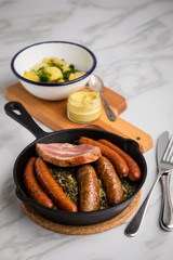 Oldenburger Grünkohl mit Pinkel, Kohlwurst, Kassler Schweine Nacken, Senf und Kartoffeln in Gusseisen Pfanne auf Marmor Tisch