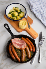 Oldenburger Grünkohl mit Pinkel, Kohlwurst, Kassler Schweine Nacken, Senf und Kartoffeln in Gusseisen Pfanne auf Marmor Tisch