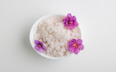 An oval white bowl with pink salt and violet flowers stands on a white background