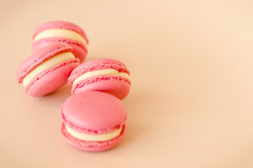 Fototapeta premium Four pink macaroon cookies with white chocolate cream on beige background