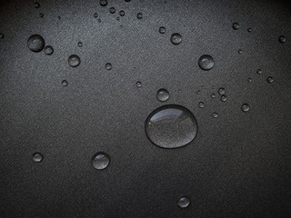 water droplets of different sizes on a dark metal surface