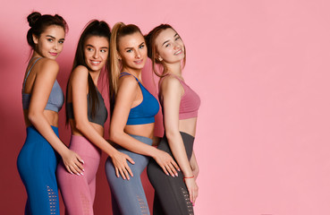 Portrait of standing behind each other athletic women in blue, grey, brown training suits on pink background