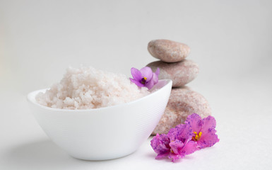 White bowl with pink salt, flowers and stones on a white background.