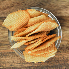 Corrugated potato chips on a wooden board. Snack, junk food. Close up.