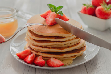 Homemade traditional American pancakes with honey or syrup and berries on a white wooden background. Breakfast, snack or dessert