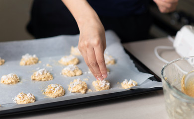 Woman making coconut cookies dough and aranging them on a pan covered with baking paper