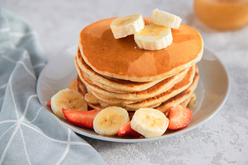 Fresh homemade pancakes with fruits on a white plate on a light background. Traditional breakfast or dessert.