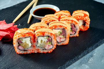 Appetizing sushi roll in tobiko caviar with cucumber, salmon, shrimp and tuna on a black board on a gray background