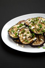 Homemade Grilled Eggplant with Feta and Herbs on a white plate on a black background, side view.