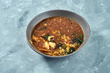 Traditional asian miso soup with udon and chicken and seaweed in a gray plate on a gray background